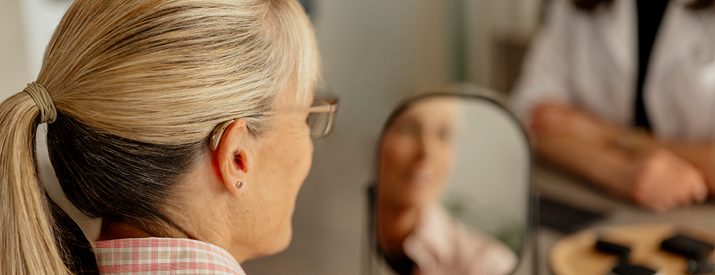 Image of side profile of woman wearing a behind-the-ear hearing aid looking at her hearing care professional